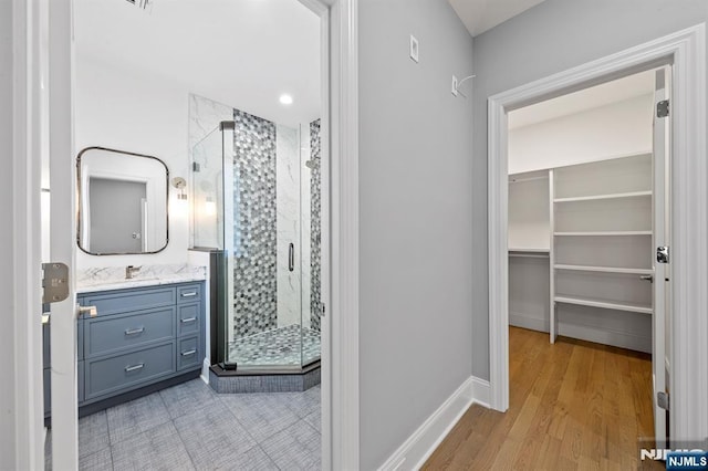 full bathroom with a spacious closet, a shower stall, vanity, wood finished floors, and baseboards