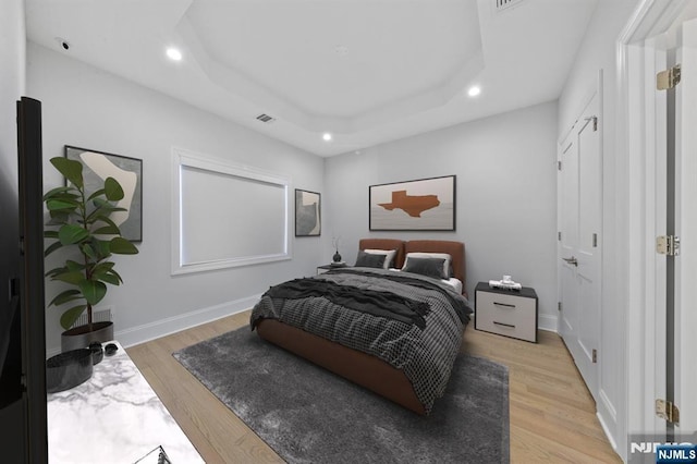 bedroom with light wood-style flooring, visible vents, a raised ceiling, and baseboards