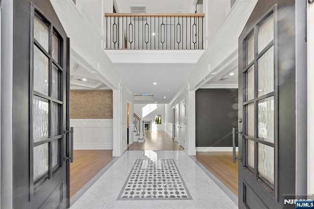 foyer with crown molding, a decorative wall, a towering ceiling, wainscoting, and stairs