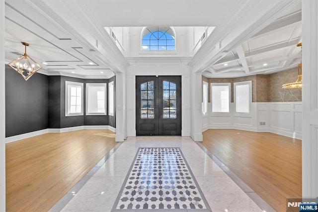 foyer entrance featuring a decorative wall, baseboards, french doors, an inviting chandelier, and crown molding