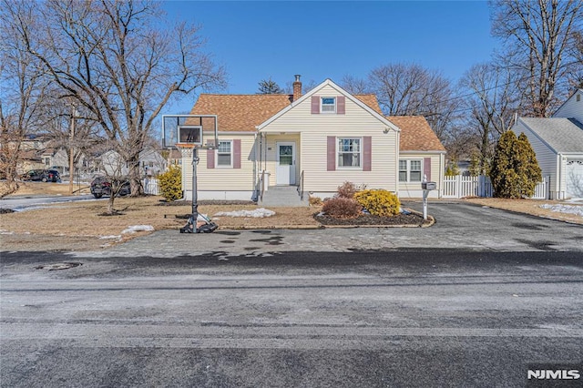 view of front facade with driveway, a shingled roof, a chimney, and fence