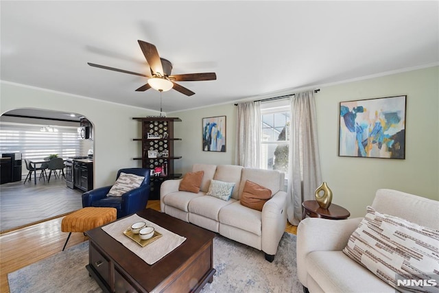 living room featuring light wood-style flooring, arched walkways, ceiling fan, and crown molding