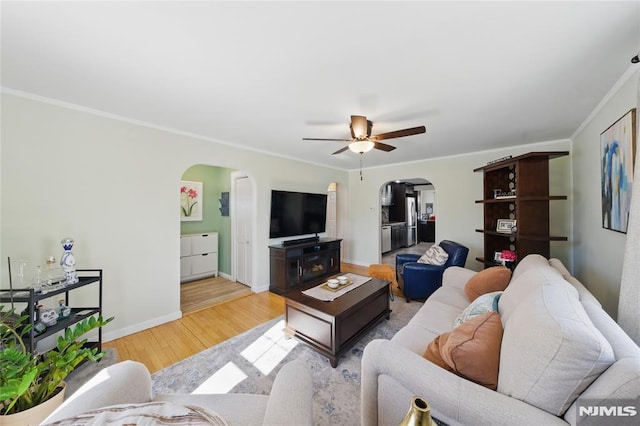 living room with baseboards, arched walkways, ceiling fan, wood finished floors, and crown molding