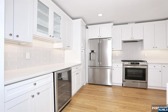 kitchen with stainless steel appliances, light countertops, white cabinetry, light wood-type flooring, and beverage cooler