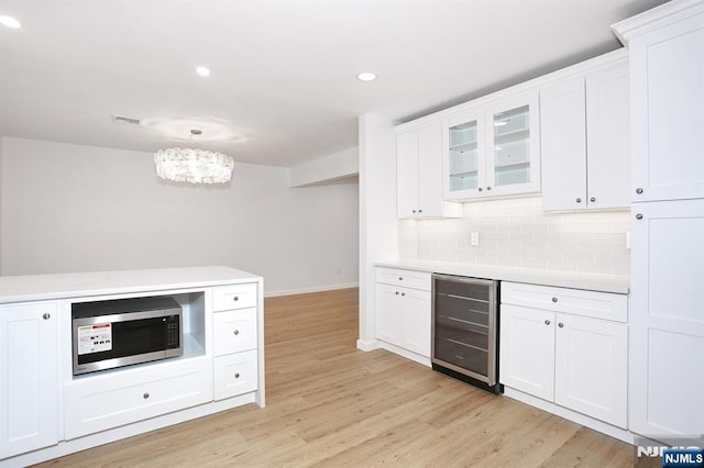 kitchen featuring light countertops, stainless steel microwave, backsplash, light wood-style floors, and beverage cooler