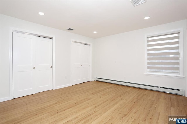 unfurnished bedroom with light wood finished floors, baseboard heating, two closets, and visible vents