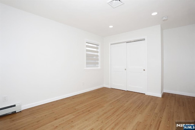 unfurnished bedroom with a baseboard heating unit, baseboards, visible vents, and light wood finished floors