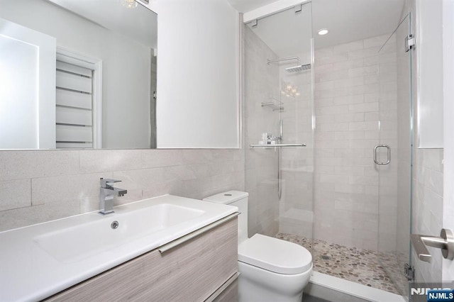 bathroom with tasteful backsplash, toilet, vanity, a shower stall, and tile walls