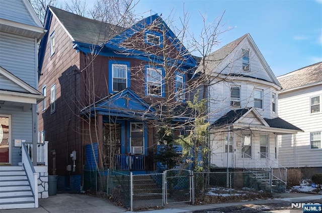 view of front facade featuring a porch, a fenced front yard, a shingled roof, and a gate