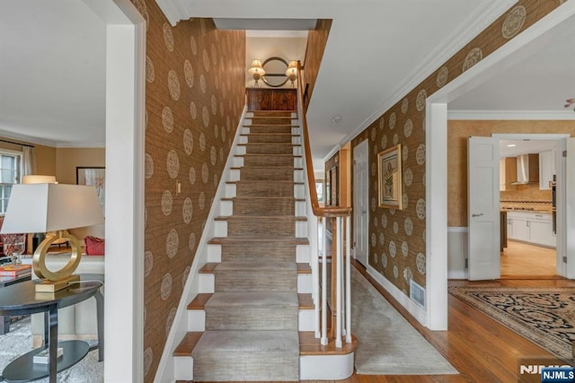 stairway featuring ornamental molding, wood finished floors, baseboards, and wallpapered walls