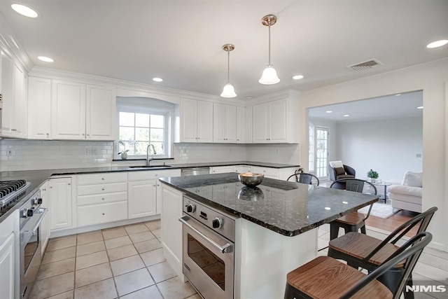 kitchen with a kitchen bar, stainless steel oven, white cabinets, and a sink