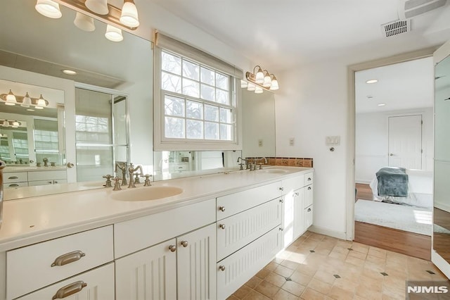 bathroom with double vanity, a shower with shower door, a sink, and visible vents