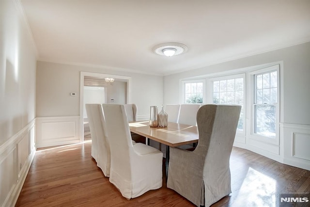 dining area with ornamental molding, wainscoting, a decorative wall, and light wood-style flooring