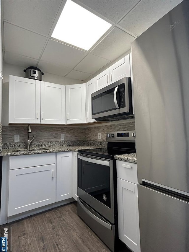 kitchen featuring a paneled ceiling, stainless steel appliances, dark wood-type flooring, a sink, and white cabinets