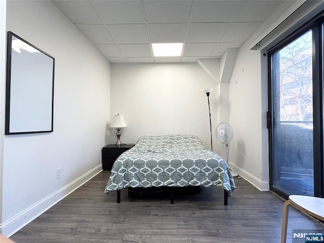 bedroom featuring access to exterior, a drop ceiling, baseboards, and wood finished floors