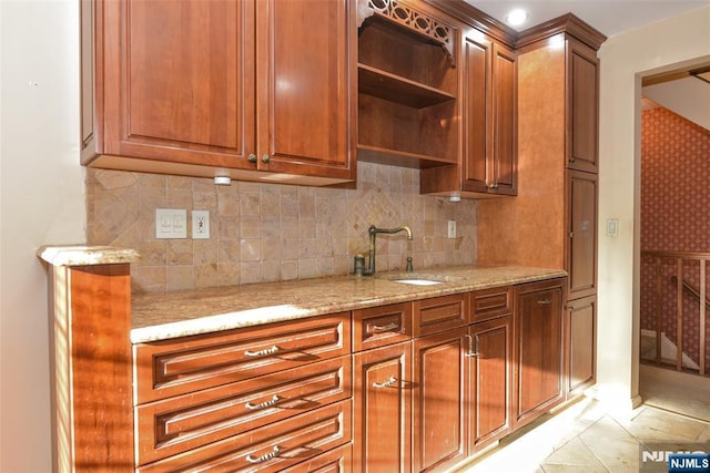 kitchen featuring a sink, light stone counters, open shelves, brown cabinetry, and decorative backsplash