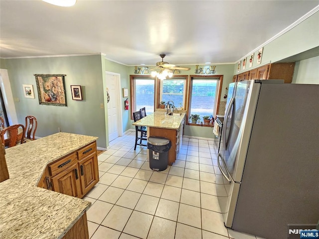 kitchen with light tile patterned floors, a center island with sink, brown cabinetry, freestanding refrigerator, and a sink