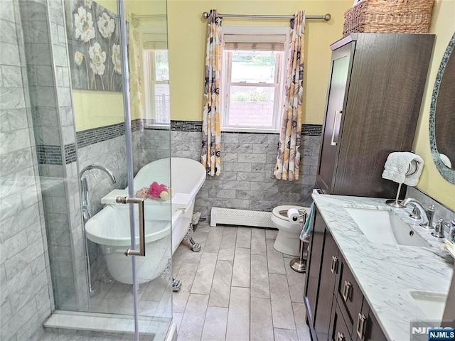 full bath with double vanity, a wainscoted wall, a sink, a freestanding bath, and tile walls