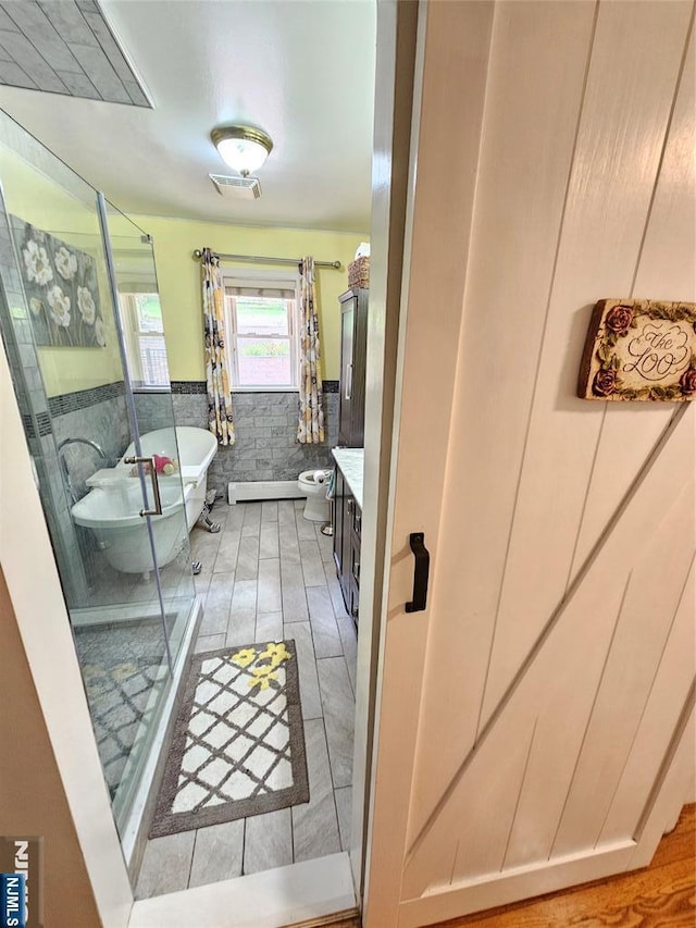 bathroom featuring a wainscoted wall, tile walls, vanity, a shower stall, and a freestanding tub