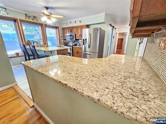 kitchen with a barn door, appliances with stainless steel finishes, brown cabinets, and ornamental molding