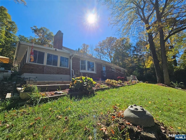 rear view of property with a yard, brick siding, and a chimney