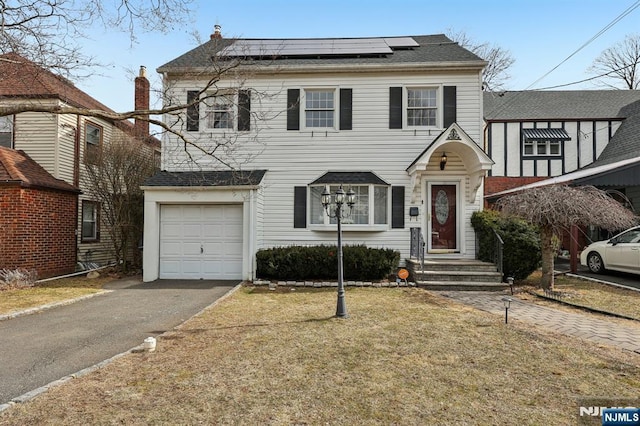 view of front of home with a garage, a front lawn, aphalt driveway, and solar panels