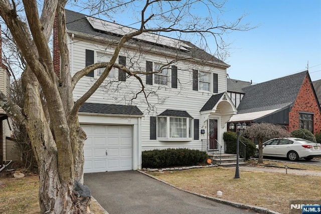 view of front of home with aphalt driveway, roof with shingles, an attached garage, and solar panels