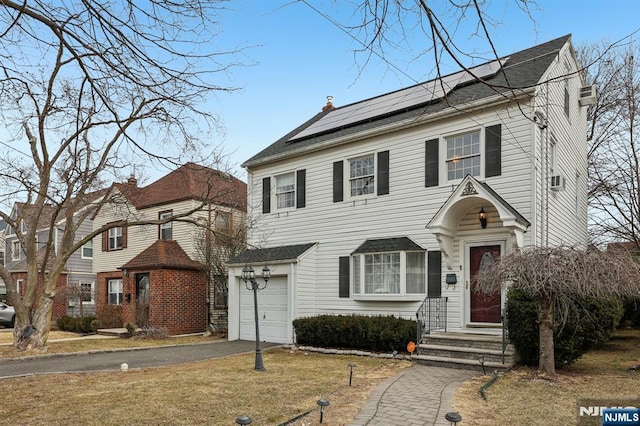 view of front of property featuring solar panels, aphalt driveway, a chimney, and a front yard