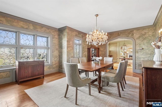 dining space featuring arched walkways, ornamental molding, wood finished floors, and wallpapered walls