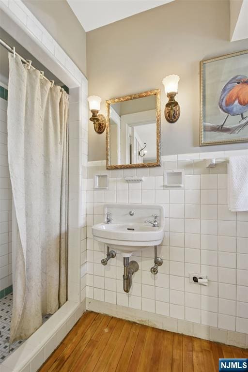 full bathroom featuring a wainscoted wall, tile walls, a sink, a shower stall, and wood finished floors