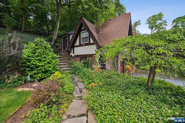 view of home's exterior featuring roof with shingles, brick siding, stairway, and stucco siding