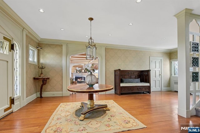 sitting room featuring light wood-style flooring, crown molding, baseboards, a lit fireplace, and wallpapered walls