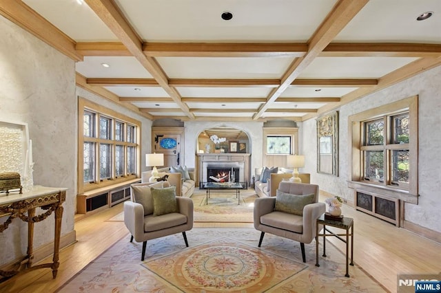 sitting room with a warm lit fireplace, coffered ceiling, baseboards, light wood-type flooring, and beam ceiling