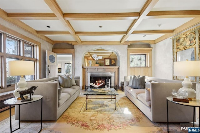 living area featuring a warm lit fireplace, coffered ceiling, and beam ceiling