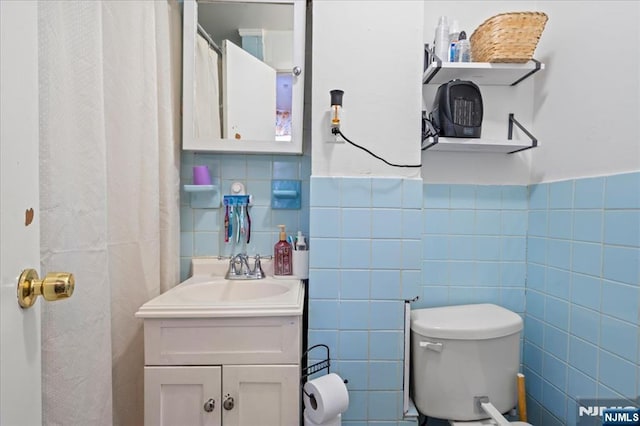 bathroom with toilet, vanity, and tile walls