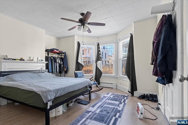 bedroom featuring a ceiling fan, a baseboard radiator, baseboards, and wood finished floors