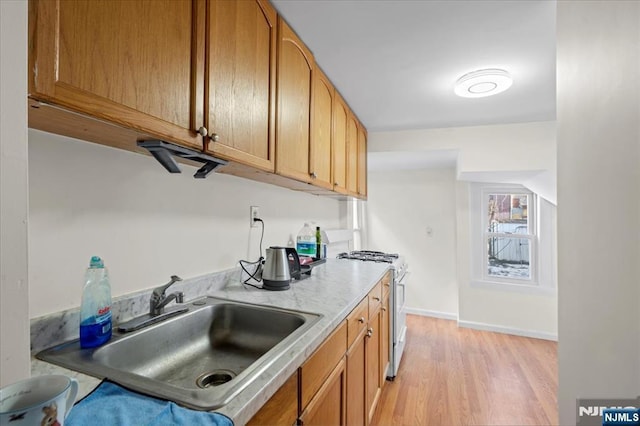 kitchen featuring a sink, baseboards, light wood-style floors, light countertops, and gas range gas stove