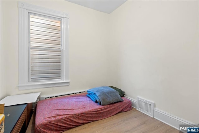 bedroom featuring a baseboard heating unit, wood finished floors, visible vents, and baseboards