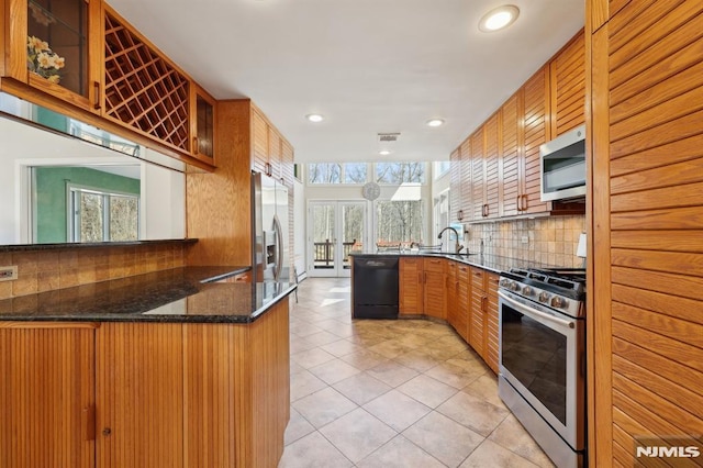 kitchen featuring backsplash, glass insert cabinets, appliances with stainless steel finishes, a peninsula, and a sink