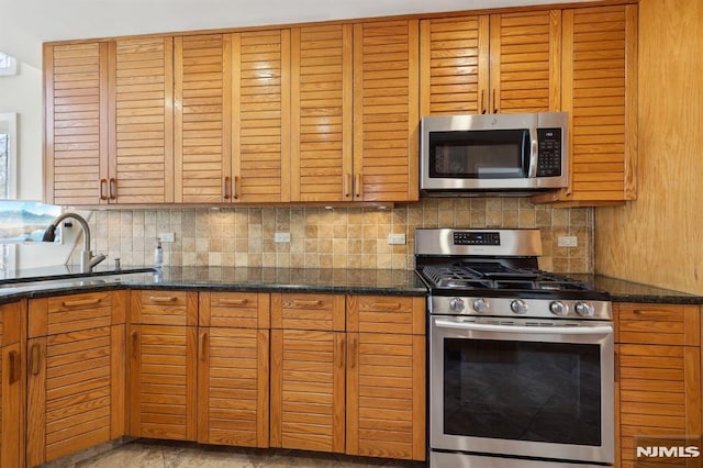 kitchen featuring dark stone counters, tasteful backsplash, appliances with stainless steel finishes, and a sink