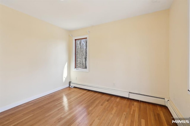 unfurnished room with a baseboard heating unit, baseboards, and wood finished floors