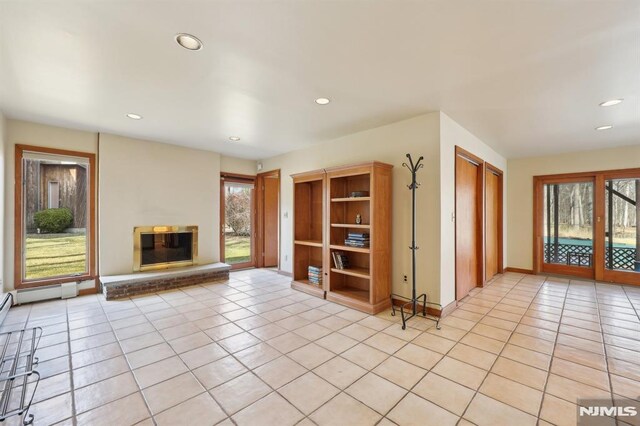 unfurnished living room with a glass covered fireplace, light tile patterned floors, recessed lighting, and baseboards