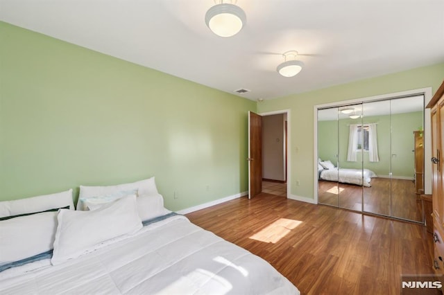 bedroom with a closet, visible vents, baseboards, and wood finished floors