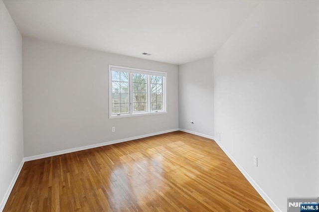 unfurnished room with wood finished floors, visible vents, and baseboards