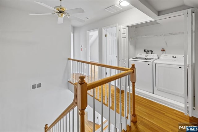 corridor featuring light wood-type flooring, washing machine and dryer, visible vents, and an upstairs landing