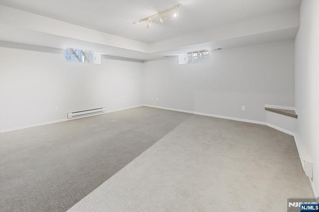 below grade area with carpet, baseboards, baseboard heating, and track lighting