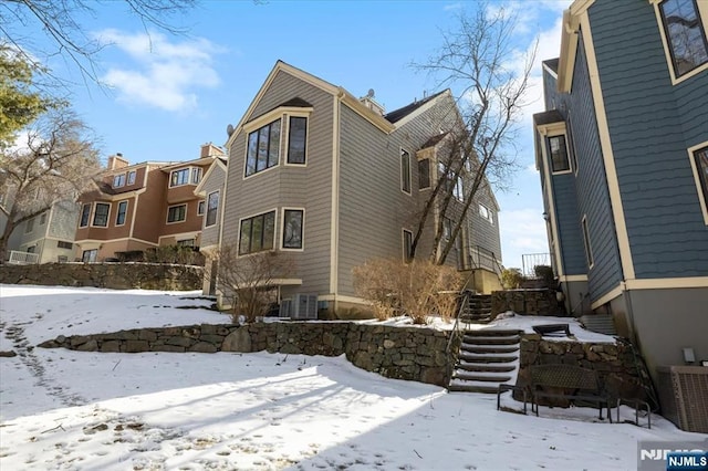 view of snow covered exterior featuring central AC and stairway