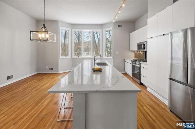 kitchen featuring an island with sink, light wood-style flooring, appliances with stainless steel finishes, white cabinetry, and a sink