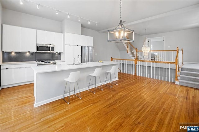 kitchen with a chandelier, a breakfast bar, a sink, appliances with stainless steel finishes, and light wood finished floors