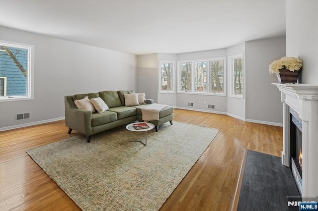 living room with a fireplace with flush hearth, visible vents, baseboards, and wood finished floors